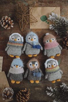 several knitted penguins sitting next to pine cones on a wooden table with snowflakes