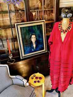 a woman's red dress is displayed in front of a painting and two chairs