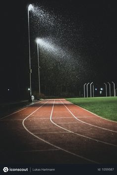 an empty running track at night with rain falling on the ground and street lights in the background