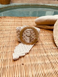 a straw hat and some knitting needles on a table next to a pool with water in the background