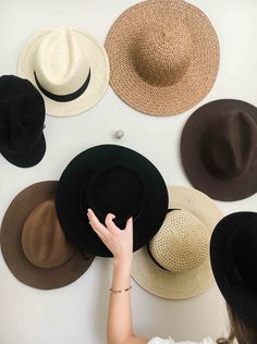 a woman looking at several hats on the wall in front of her, with one hand touching the hat