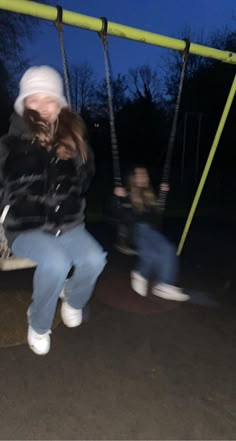 a woman sitting on a swing at night with two other people in the back ground