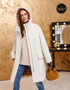 a woman in a white coat is holding a handbag and smiling at the camera