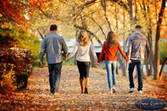 three people walking down a leaf covered path holding hands