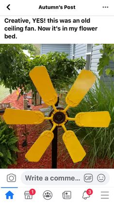 a yellow fan sitting on top of a wooden pole in front of a tree and bushes