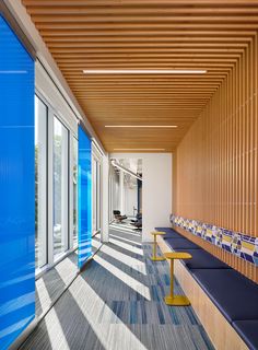 an empty room with blue benches and wooden slats on the wall, along with large windows