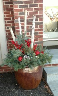 a potted plant with red berries and pine cones in front of a brick building