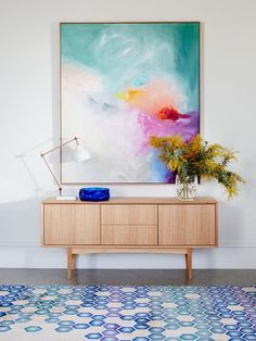 a painting hanging on the wall next to a wooden cabinet with vases and flowers