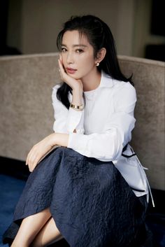 a woman sitting on top of a couch wearing a white shirt and black skirt with her hand under her chin