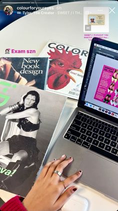 a woman's hand on the keyboard of a laptop computer next to magazines and magazines