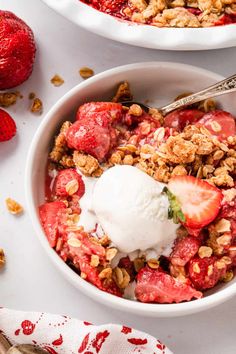 two bowls filled with strawberries and granola on top of a white tablecloth