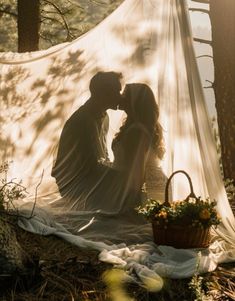 a man and woman sitting in the woods under a white tarp with flowers on it