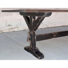 an old wooden table sitting on top of a cement floor next to a white brick wall