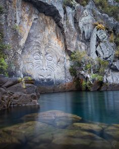 a rock face carved into the side of a cliff next to a body of water