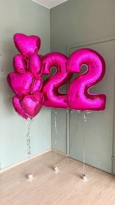 large pink balloon shaped like the number twenty two in front of a wall with balloons attached to it