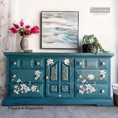 a blue dresser with flowers painted on the front and side panels, in a room