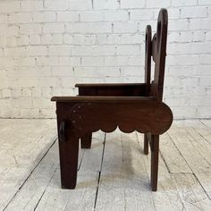 an old wooden chair with scalloped back and foot rests against a white brick wall