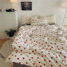 a bed with red hearts on it in a room next to a white dresser and lamp