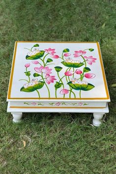 a white box with pink flowers painted on it sitting in the middle of some grass