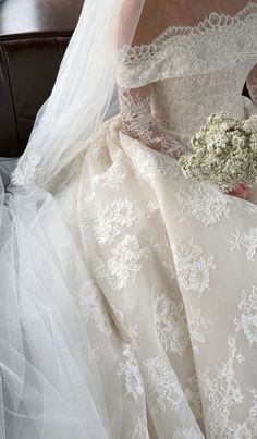 a woman in a wedding dress sitting on a chair holding a bouquet of white flowers