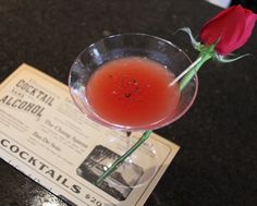 a red rose sitting in a martini glass on top of a table next to a newspaper