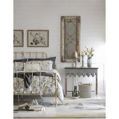 a bedroom with white walls and paintings on the wall, including an antique iron bed