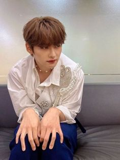 a young man sitting on top of a bed wearing blue pants and a white shirt