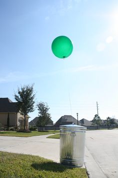 a green balloon flying over a trash can