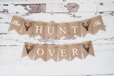 two burlap banners with deer heads and the words hunt over are hung on an old wooden wall