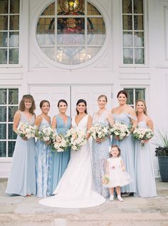 a group of women standing next to each other in front of a white door holding bouquets