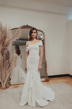 a woman standing in front of a mirror wearing a white dress