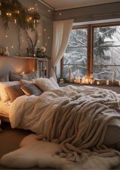 a bed with blankets and candles in front of a window filled with snow covered trees