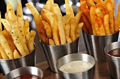 french fries and dipping sauces in metal cups on a wooden table at a restaurant