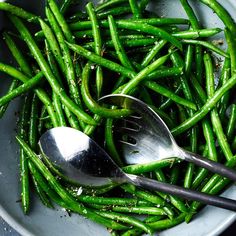 a bowl filled with green beans and two spoons