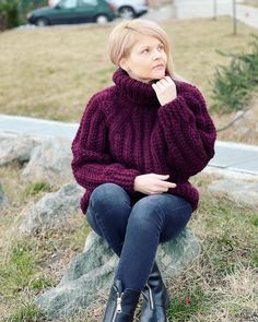 a woman sitting on top of a rock wearing a purple sweater and black booties