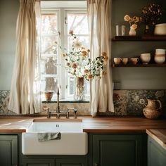 a kitchen sink sitting under a window next to a counter top with flowers in it