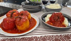 two plates with stuffed peppers and mashed potatoes are on a table next to wine glasses