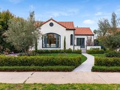 a white house with hedges in front of it and bushes around the entrance to the home