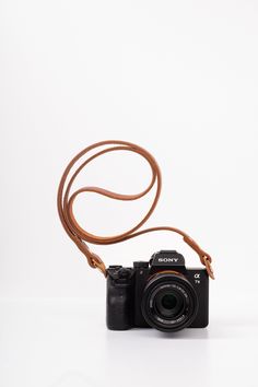 a camera sitting on top of a white table next to a brown strap with a black lens