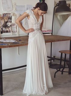 a woman standing in front of a table wearing a white dress with lace on it