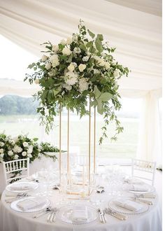 a table with white flowers and greenery on it is set for a formal function