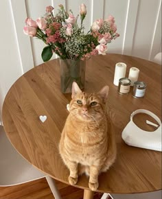 a cat sitting on top of a wooden table next to a vase filled with flowers