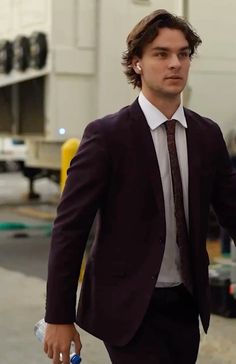 a man wearing a suit and tie walking down the street with his hand in his pocket