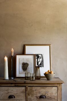 a wooden dresser topped with framed pictures and candles next to oranges on top of it