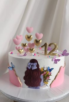 a white cake with pink frosting and gold numbers on it, decorated with hearts