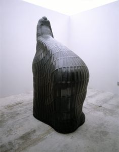 a large black sculpture sitting on top of a cement floor next to a white wall