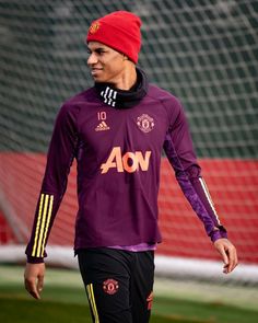 a man in a red hat and purple shirt is on the soccer field with his foot