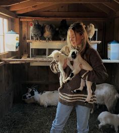 a woman holding two puppies in her arms while standing next to other dogs and chickens