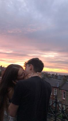 a man and woman are kissing in front of the sun setting over some rooftops