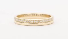 a yellow gold wedding ring with channeled diamonds on the side and inside, set against a white background